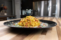 Spaghetti Carbonara Golden Spaghetti Carbonara twisted high on a black plate with bacon bits and grated cheese