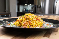 Spaghetti Carbonara Mounded Spaghetti Carbonara with bacon bits, herbs, and grated cheese on a black plate.