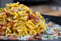 Spaghetti Carbonara Close-up of Spaghetti Carbonara piled high with crispy bacon, chives, and grated cheese on a dark plate.