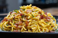 Spaghetti Carbonara A mound of Spaghetti Carbonara with crispy bacon, chives, and grated cheese on a dark plate.