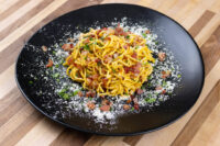 Spaghetti Carbonara Plate of Spaghetti Carbonara with crispy bacon bits, grated cheese, and herbs on black plate.