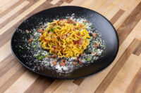 Spaghetti Carbonara Black plate of Spaghetti Carbonara with bacon bits, herbs, and grated cheese on a wooden table