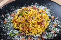 Spaghetti Carbonara Plate of Spaghetti Carbonara with bacon bits, herbs, and grated cheese on a black dish.