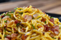 Spaghetti Carbonara Close-up of Spaghetti Carbonara with crispy bacon bits, chives, and grated cheese on a dark plate