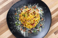 Spaghetti Carbonara Spaghetti Carbonara twirled on a black plate, coated in yellow sauce with crispy bacon, cheese, and herbs
