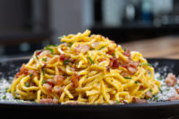 Spaghetti Carbonara Golden Spaghetti Carbonara piled high with crispy bacon, chives, and grated cheese on a black plate.