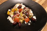Greek Salad Black plate of Greek Salad with diced tomatoes, peppers, red onion, olives, and crumbled feta.