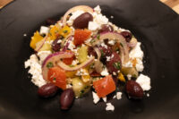 Greek Salad Greek Salad with crumbled feta, kalamata olives, red onion, and tomato on a black plate