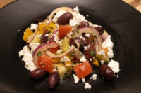Greek Salad Greek Salad with feta, olives, red onion, tomato, cucumber and peppers on a black plate