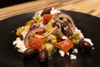 Greek Salad Greek Salad with feta, kalamata olives, tomatoes, red onion and peppers on a black plate.