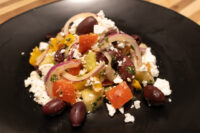 Greek Salad Black plate of Greek Salad with tomato, pepper, red onion, olives and crumbled feta.