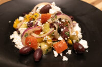 Greek Salad Greek Salad on a black plate with kidney beans, tomato, red onion, olives and crumbled feta.