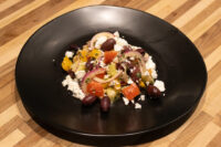 Greek Salad Greek Salad with feta, olives, red onion and diced peppers plated on a black dish on a wood table.