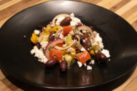 Greek Salad Greek Salad with tomatoes, peppers, red onion, kalamata olives and feta on a black plate.