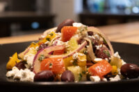 Greek Salad Greek Salad with diced peppers, red onion, olives, and crumbled feta on a dark plate.