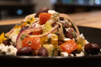 Greek Salad Close-up of Greek Salad with diced peppers, red onion, feta, and olives on a dark plate.