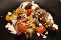Greek Salad Greek Salad on a black plate with feta, olives, onion, tomato and peppers