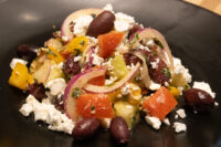 Greek Salad Chopped Greek Salad with feta, kalamata olives, tomato, and red onion on a black plate.