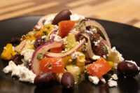 Greek Salad Greek Salad on a black plate with peppers, red onion, black olives, and crumbled feta cheese.