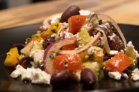 Greek Salad Close-up of Greek Salad with tomato chunks, red onion slices, black olives, and feta on a black plate.