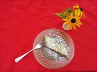 Apple Strudel A slice of Apple Strudel dusted with powdered sugar on a glass plate with a fork, beside yellow flowers.