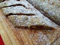 Apple Strudel Sliced Apple Strudel on a wooden board, dusted with powdered sugar, filling visible in the cut sections