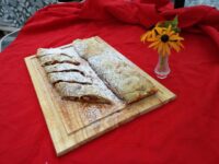 Apple Strudel Sliced Apple Strudel dusted with powdered sugar on a wooden board, red cloth and yellow flowers behind