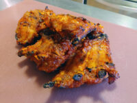 Czech BBQ – Honey Pork Ribs Charred, glazed Czech BBQ – Honey Pork Ribs with red-orange honey sauce on a pink cutting board.