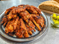 Stacked Czech BBQ – Honey Pork Ribs on a metal plate with crusty bread and a bowl of dill pickles.