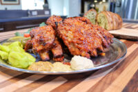 Czech BBQ Honey Pork Ribs Glazed Czech BBQ – Honey Pork Ribs on a metal plate with pickles, mustard dollops, and bread.