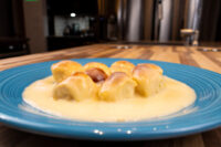 Golden Little Buns with Vanilla Pudding (Buchticky s Krémem) clustered together in a pool of pale custard on a teal plate, with a dim kitchen blurred behind.
