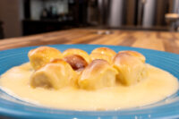 Golden Little Buns with Vanilla Pudding pieces in custard sauce, drizzled with caramel, on a blue plate.