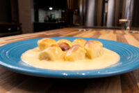 Golden Little Buns with Vanilla Pudding (Buchticky s Krémem) clustered on a blue plate, coated in cream sauce, set on a wooden table.