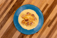 Eight browned buns arranged in a circle and covered in pale vanilla custard on a blue plate: Little Buns with Vanilla Pudding (Buchticky s Krémem).
