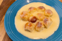 Little Buns with Vanilla Pudding (Buchticky s Krémem) - nine browned buns in custard on a blue plate.
