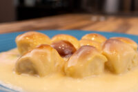 Golden yeast buns glazed with caramel sit in a pool of vanilla custard on a blue plate, this is Little Buns with Vanilla Pudding (Buchticky s Krémem)