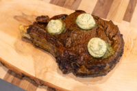 Cowboy Steak Bone-in Cowboy Steak with three pats of herb butter melting on a wooden board