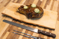 Cowboy Steak Seared bone-in Cowboy Steak topped with herb butter, resting on a live-edge wooden board with knife and fork