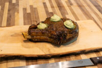 Cowboy Steak Bone-in Cowboy Steak with charred crust and three dollops of herb butter on a wooden board.