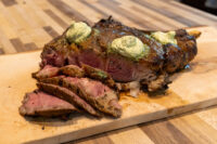 Cowboy Steak Sliced Cowboy Steak with charred crust and herb butter medallions on a wooden cutting board