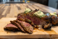 Cowboy Steak Sliced Cowboy Steak with charred crust and herb butter melting on top, on a wooden board.