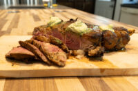 Cowboy Steak Sliced Cowboy Steak with dark seared crust and pink center, topped with herb butter on a wooden board
