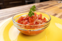 Czech Tomato Salad with Onion Glass bowl of Czech Tomato Salad with Onion, diced tomato and onion topped with parsley, on a yellow plate.