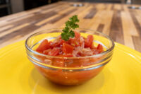 Czech Tomato Salad with Onion Glass bowl of Czech Tomato Salad with Onion, diced tomato and onion topped with parsley, on a yellow plate.