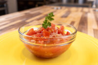 Czech Tomato Salad with Onion Glass bowl of Czech Tomato Salad with Onion, garnished with a sprig of herb, on a yellow plate.