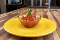 Czech Tomato Salad with Onion Small glass bowl of diced Czech Tomato Salad topped with parsley, served on a yellow plate.