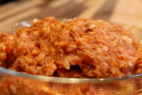 Italian Sausage Recipe Raw Italian Sausage mixture with red spice coating piled in a glass bowl on a wooden surface.