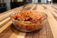 Italian Sausage Recipe Raw Italian Sausage meat mixed with reddish seasoning in a glass bowl on a wood counter