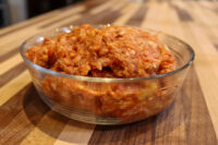 Italian Sausage Recipe Glass bowl of raw seasoned ground pork for Italian Sausage, mixed with reddish spices on a wooden table