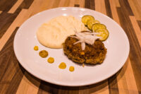 Karbenátky (Czech Burger) Breaded Karbenátky (Czech Burger) patty topped with onion, served with mashed potato and cucumber slices.